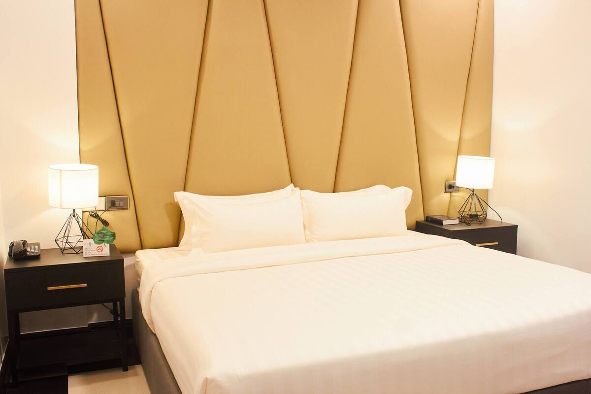 A hotel room with a bed, two bedside tables, lamps, a phone, and a sign.