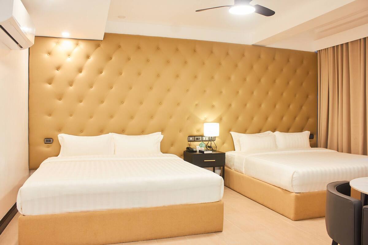 A hotel room with two beds, a tufted headboard, bedside tables with lamps, and a ceiling fan.