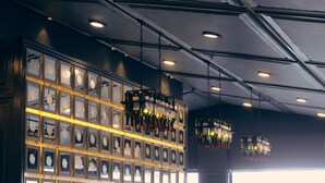 Una zona de bar con una pared de fotografías enmarcadas, un área de estar con mesas y sillas, y lámparas colgantes.