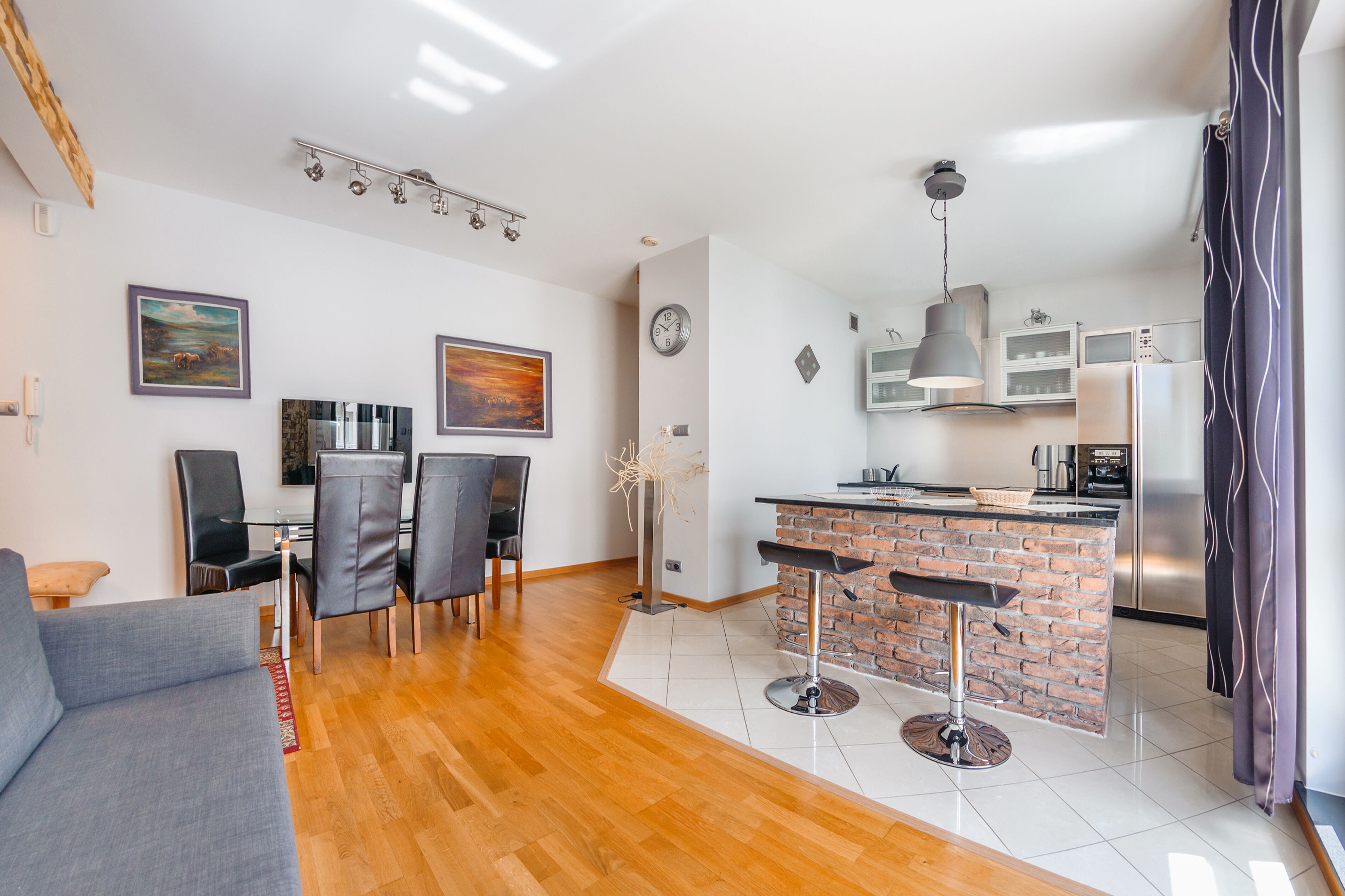 A modern kitchen with a brick island, a dining area with chairs, and a living room with a sofa.