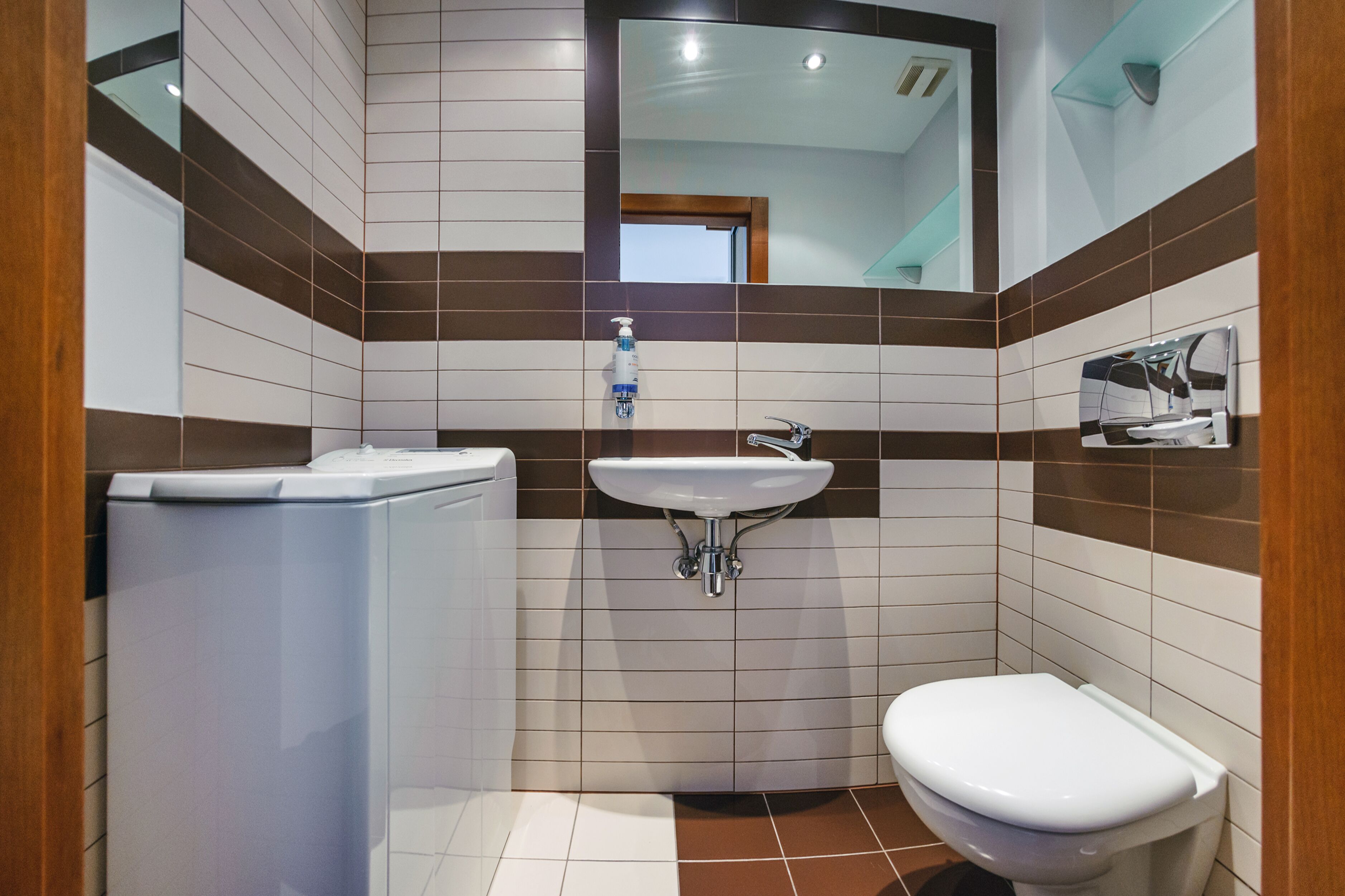 A compact bathroom with a white toilet, a sink with a mirror above it, and a washing machine.