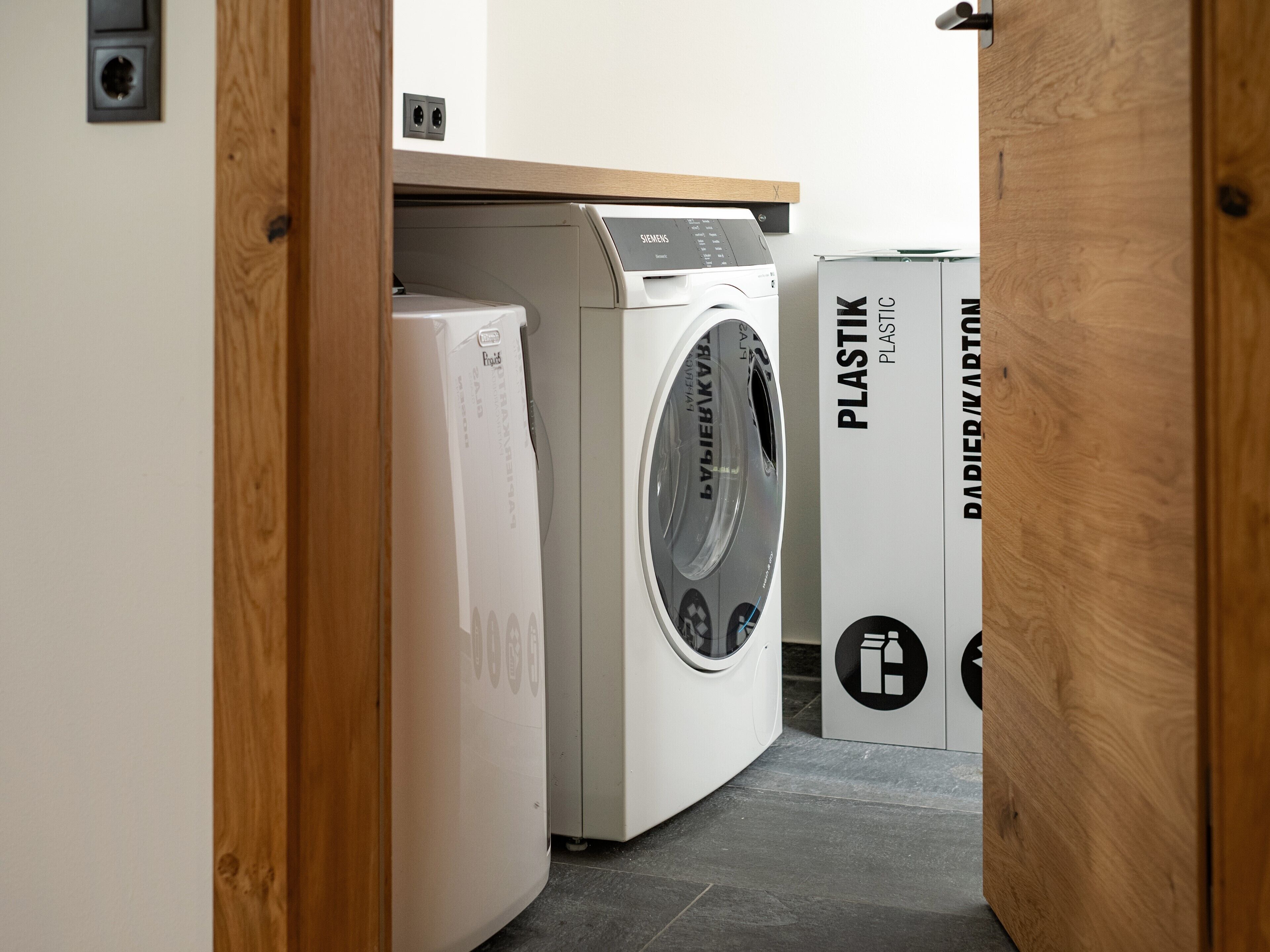 Un espace buanderie équipé d’un lave-linge et d’un sèche-linge, tous deux portant les inscriptions « PLASTIK » et « DADIER/MARTIN ».