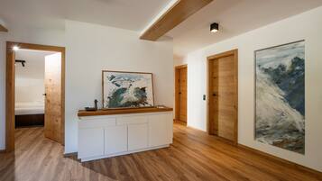 Un pasillo con suelo de madera, una consola blanca con obras de arte y puertas de madera.