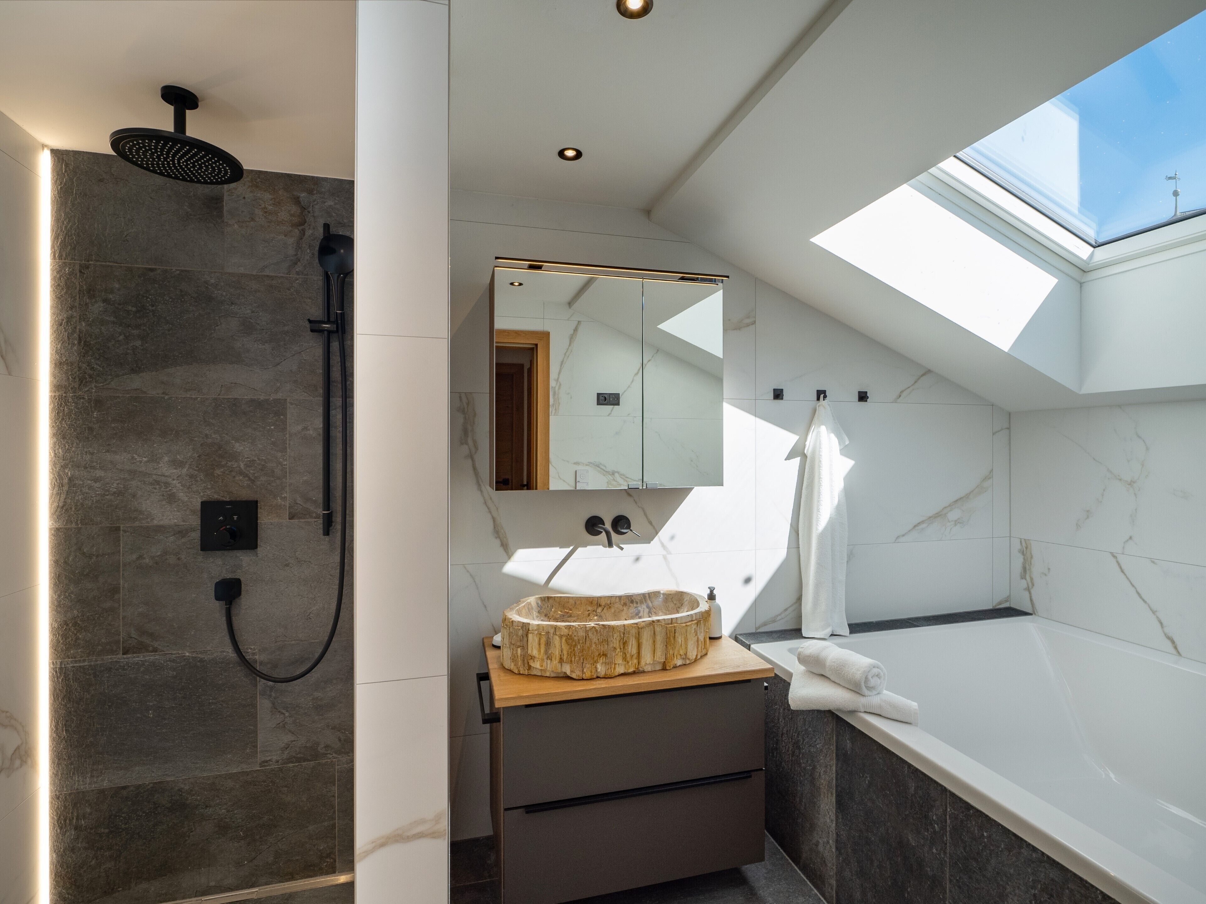 A modern bathroom with a skylight, a freestanding bathtub, a vanity with a wooden bowl sink, and a shower with a black head.
