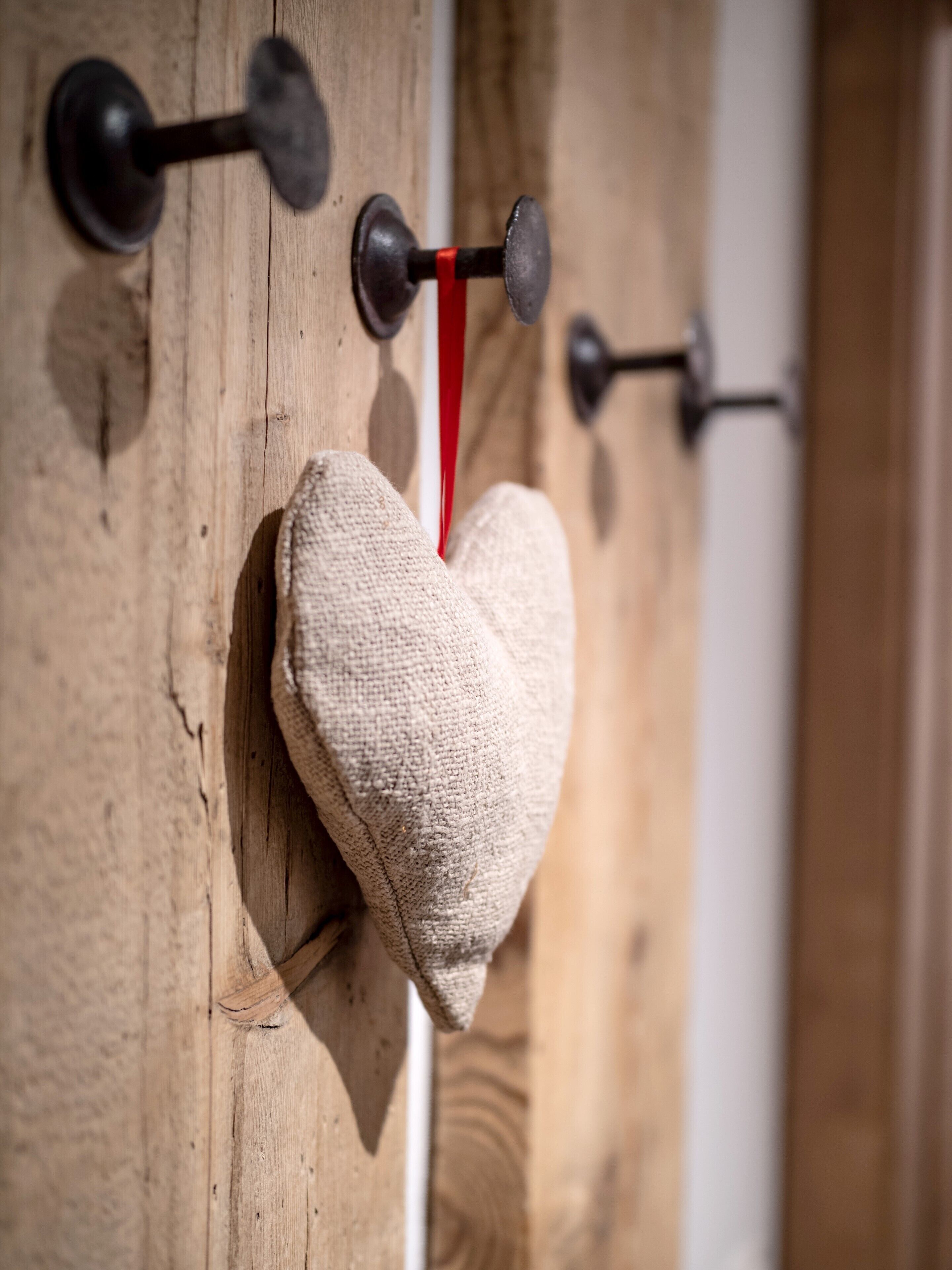 A heart-shaped fabric item hanging on a wooden wall with metal hooks.