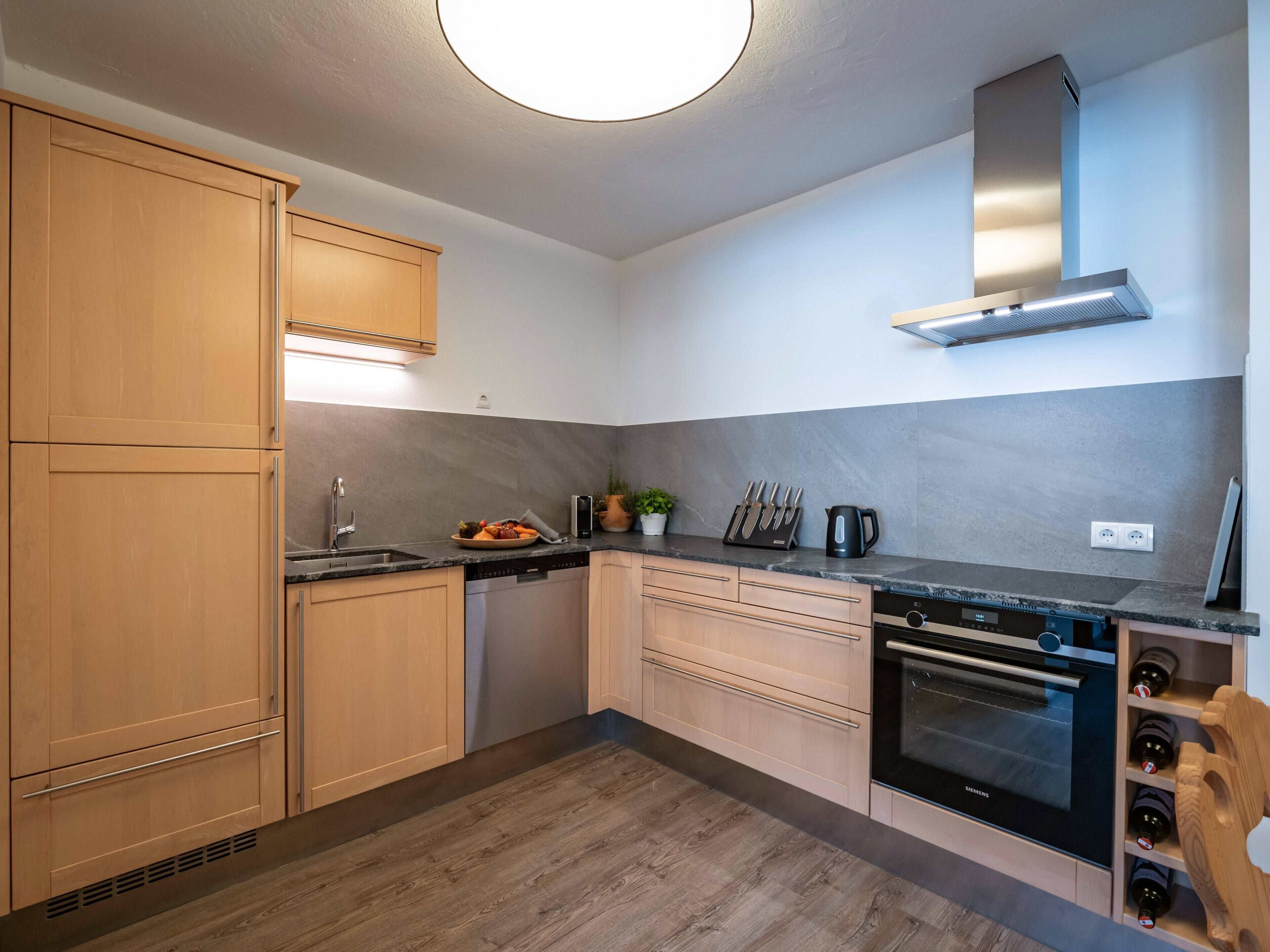 Una cocina moderna con armarios de madera, horno empotrado y campana extractora de acero inoxidable.