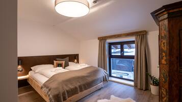 A bedroom with a wooden bed, a large window with curtains, a ceiling light, and a wooden wardrobe.