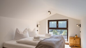 A bedroom with a bed, pillows, a blanket, a wooden cabinet, and a window with a view. - Alpine Homes - Hopfgarten Zentrum (Hopfgarten im Brixental)