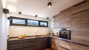 A modern kitchen with dark cabinetry, a built-in oven, and a window above the sink. - Alpine Homes - Hopfgarten Zentrum (Hopfgarten im Brixental)
