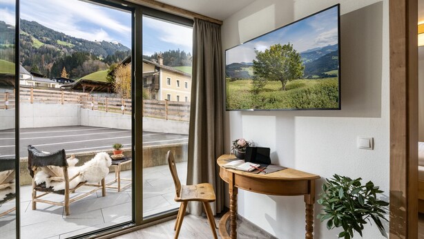 A modern room with a large window, a wooden table with a laptop, a chair, and a potted plant. - Alpine Homes - Hopfgarten Zentrum (Hopfgarten im Brixental)