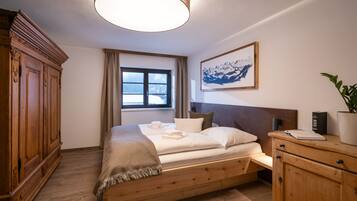 A bedroom with a wooden bed, a nightstand, a large window, a painting, and a wardrobe.