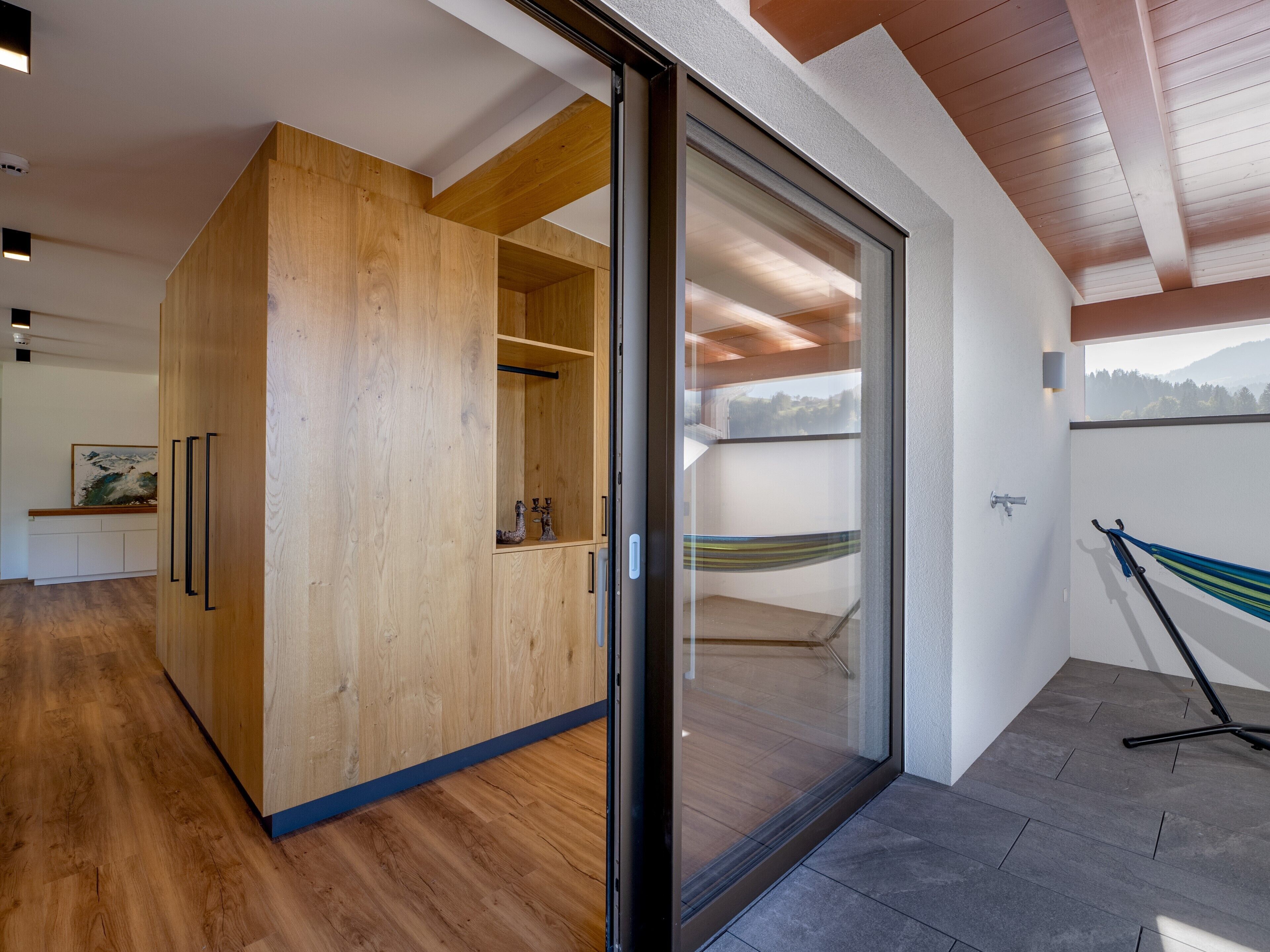 A modern interior with a wooden wardrobe, a glass door leading to a balcony, and a hammock.