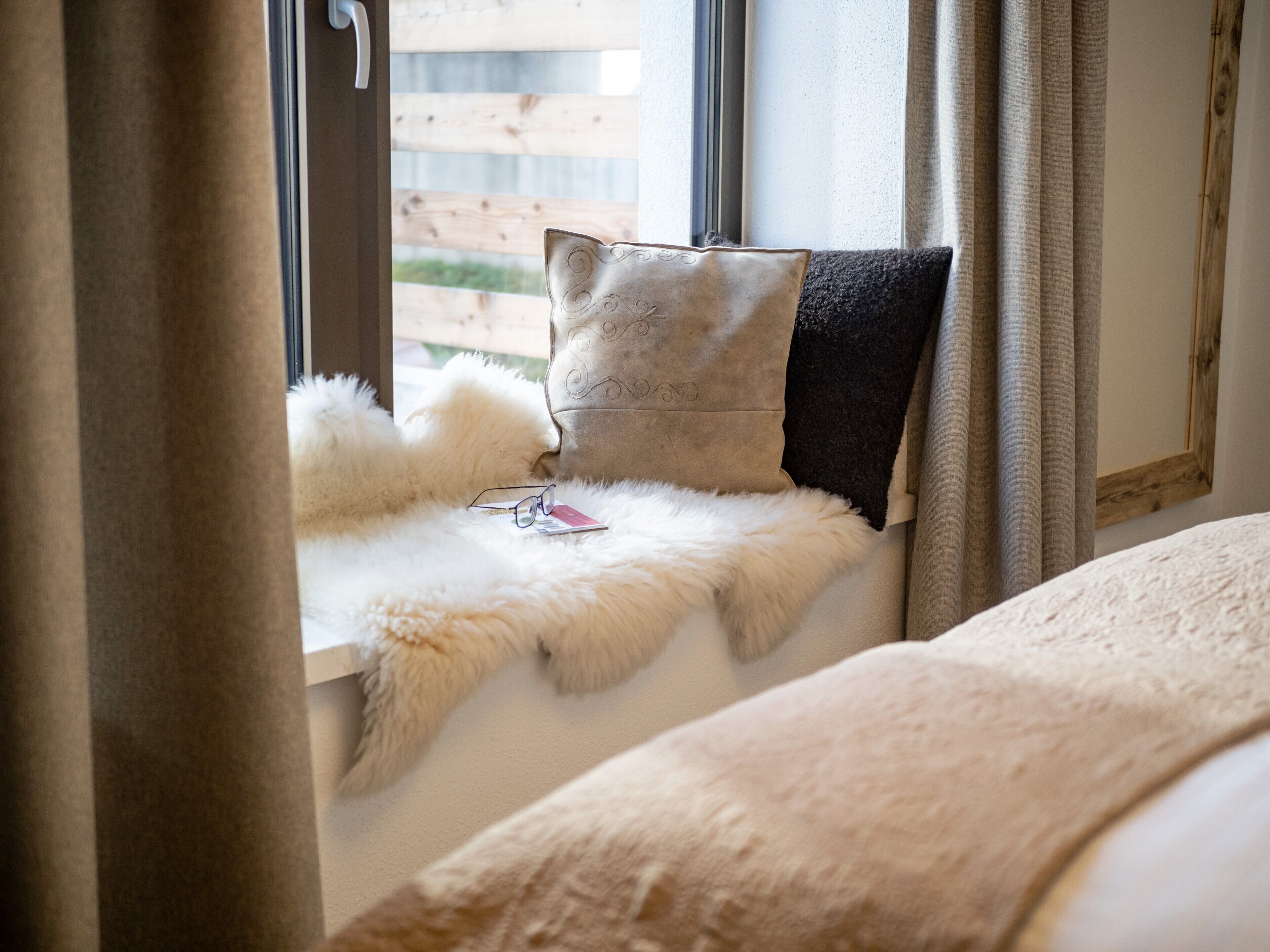 A cozy room with a fur-covered window seat, a pillow, and a pair of glasses on the seat.