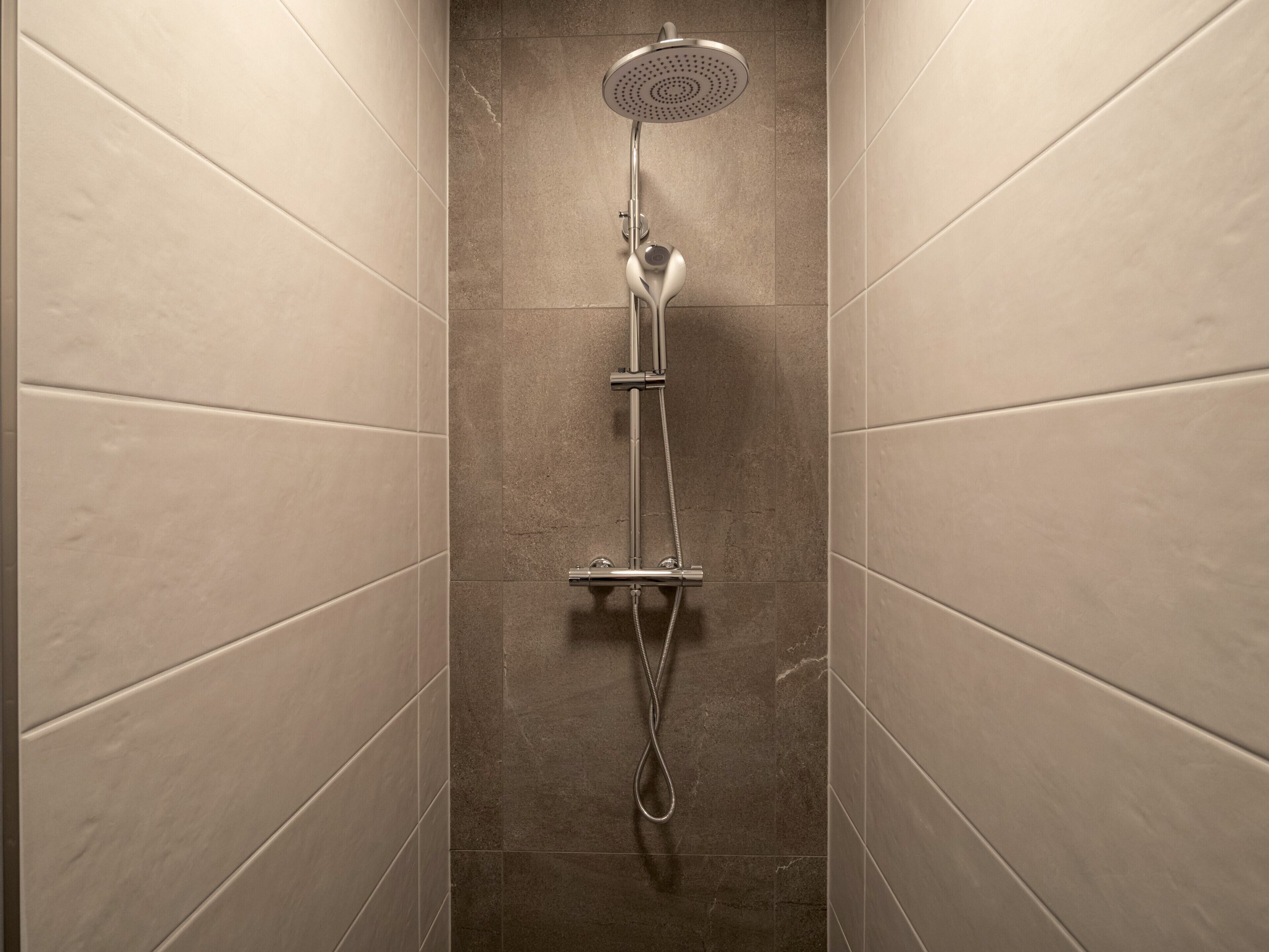 A narrow, tiled shower area with a handheld showerhead and a fixed overhead showerhead.