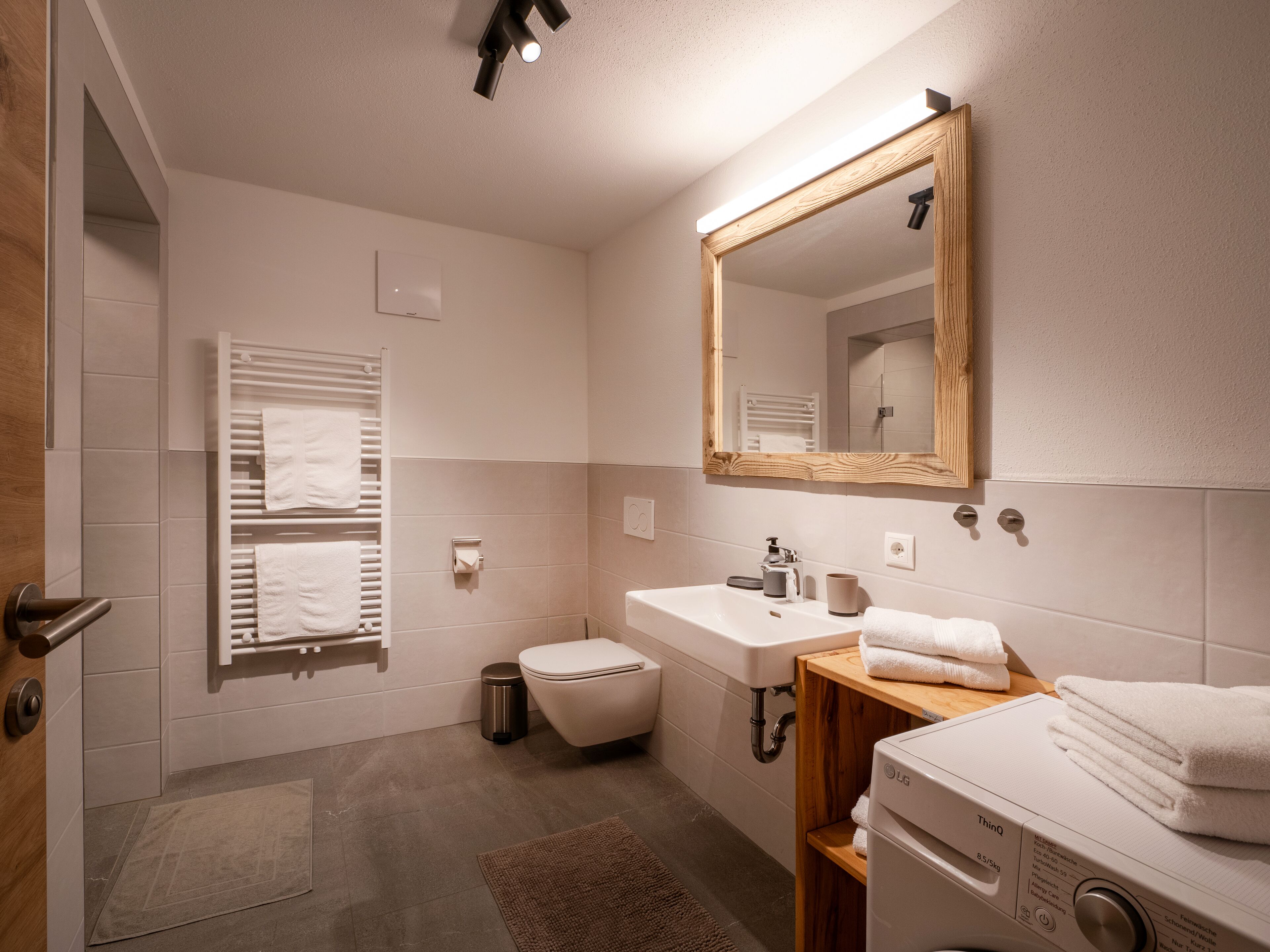 A modern bathroom with a toilet, sink, mirror, and a stack of towels.