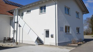 A two-story building with a white exterior, a red-tiled roof, and a staircase leading to the upper floor. - Beautiful vacation apartment in the idyllic Allgäu (Altusried)
