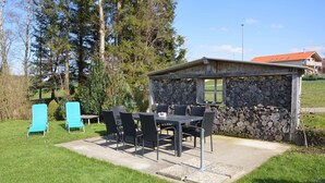 An outdoor patio with a stone wall, a table with chairs, and a small building with a window. - Beautiful vacation apartment in the idyllic Allgäu (Altusried)