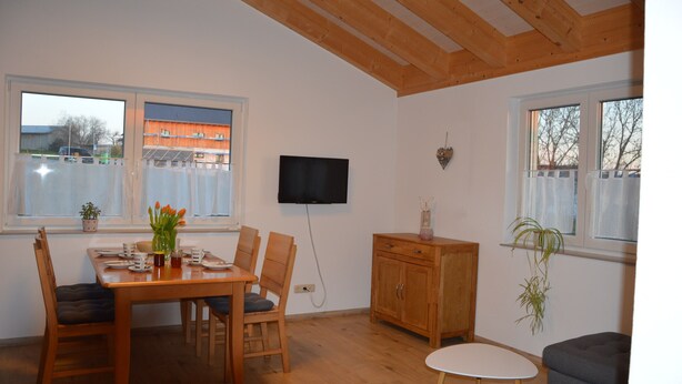 A dining area with a wooden table and chairs, a television mounted on the wall, and a small cabinet. - Beautiful vacation apartment in the idyllic Allgäu (Altusried)