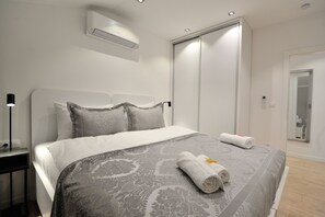 A modern hotel room with a large bed, a bedside table, an air conditioning unit, a wardrobe, and a mirror. - Solaris Apartments (Mostar)