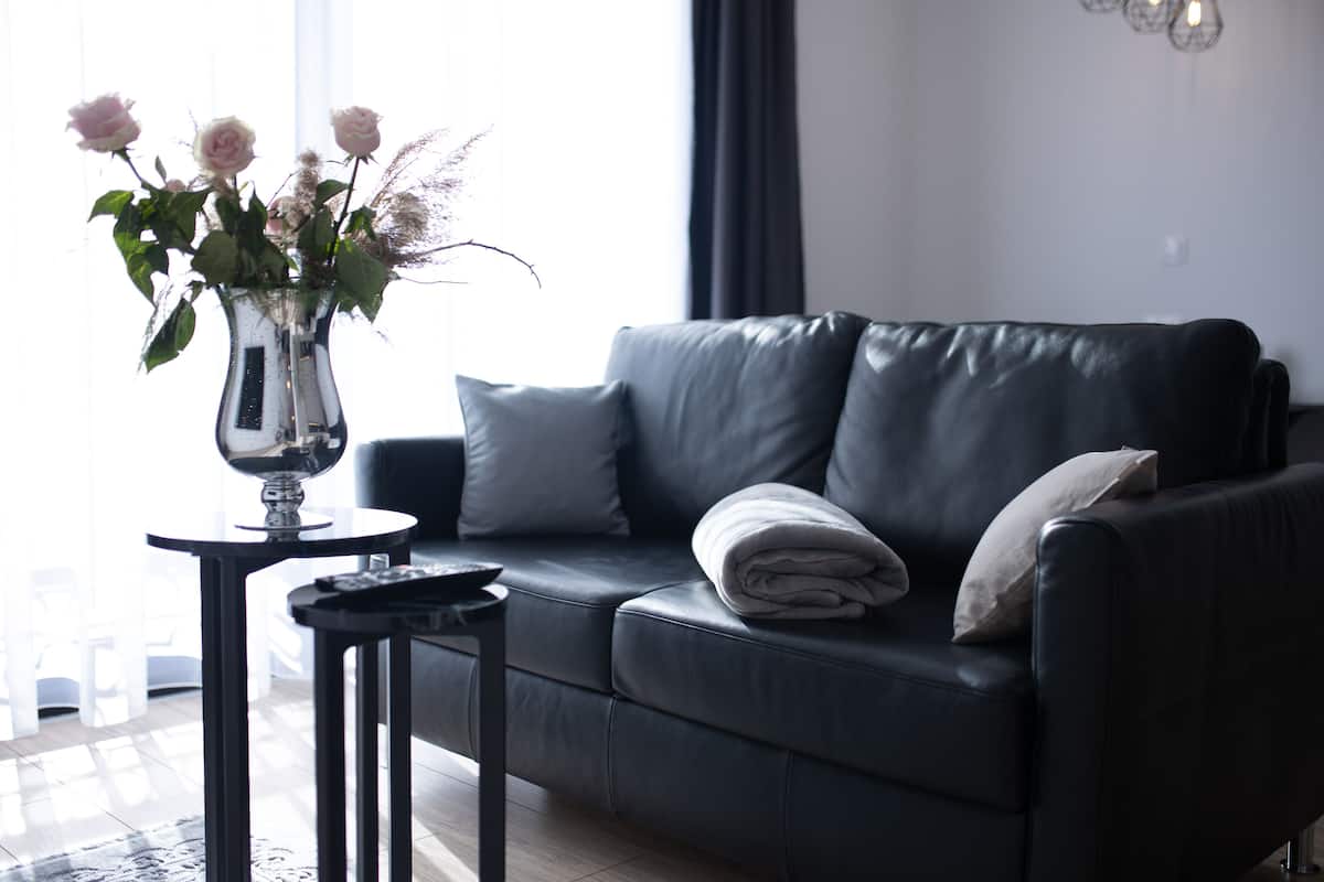 A modern living room with a black leather sofa, a small side table, and a vase with flowers.