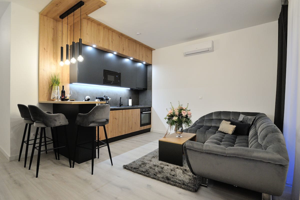 A modern kitchen with a central island, bar stools, and a grey sofa.
