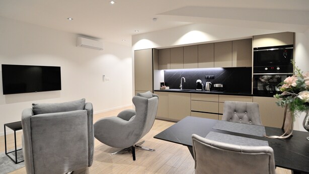 A modern kitchen with a flat-screen TV, grey upholstered chairs, and a dining table.