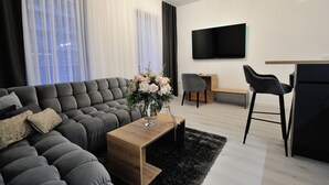 Ein modernes Wohnzimmer mit grauem Sofa, einem Holztisch, einem schwarzen Teppich, einem grauen Sessel und einem an der Wand befestigten Flachbildfernseher.