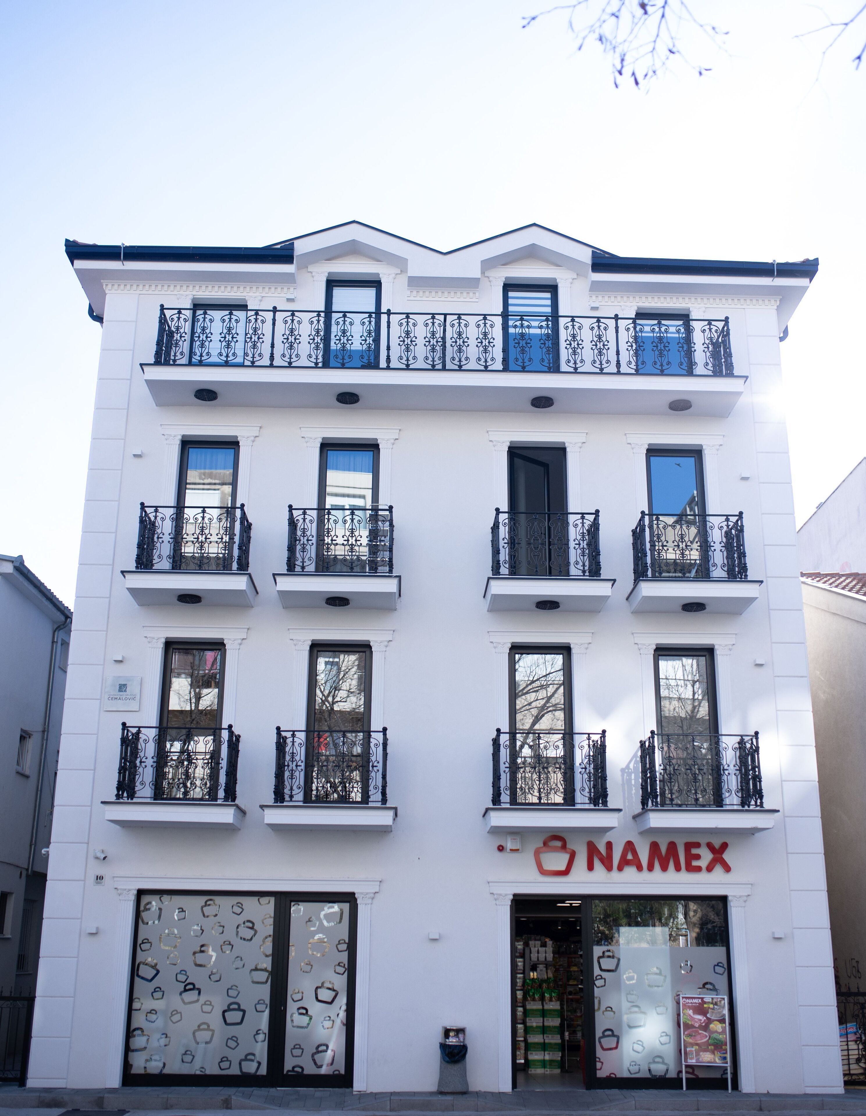 Un bâtiment blanc doté de balcons en fer forgé noir et d’une devanture avec une enseigne rouge sur laquelle on peut lire « NAMEX ».