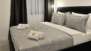 Ein modernes Schlafzimmer mit einem schwarzen Kopfteil, einer grauen, gemusterten Bettdecke und zwei aufgerollten Handtüchern auf dem Bett.