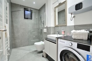 A modern bathroom with a walk-in shower, a toilet, a sink, and a washing machine. - Solaris Apartments (Mostar)