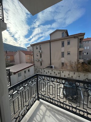 A balcony with a metal railing overlooking a residential area with buildings and a mountain in the background.