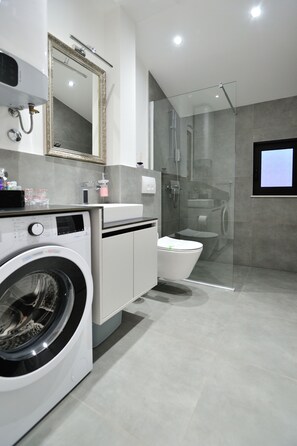 A modern bathroom with a washing machine, toilet, and glass-enclosed shower.