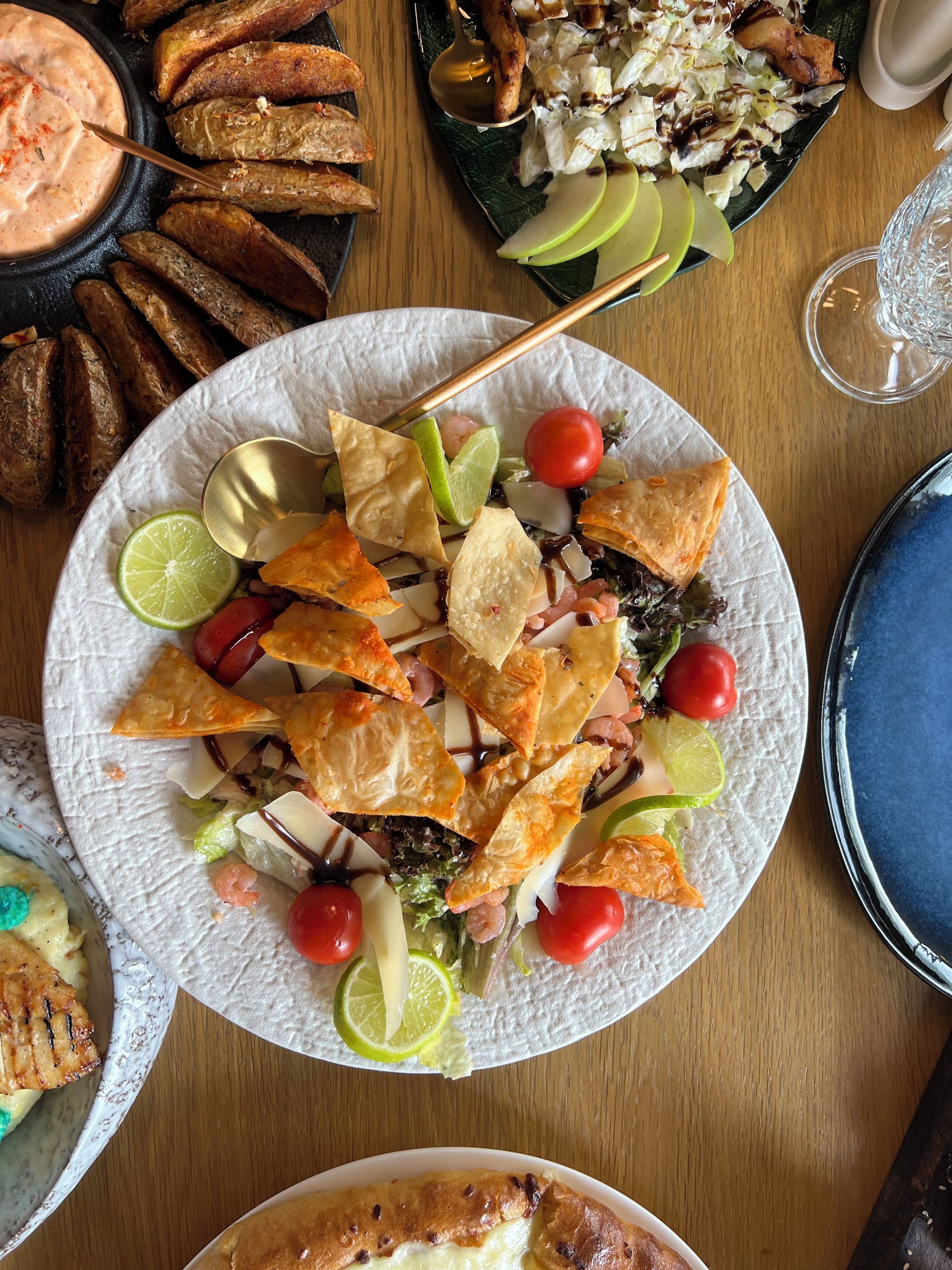 Een tafel met diverse gerechten, waaronder een bord nacho's, een bakje dip en nog andere soorten eten.