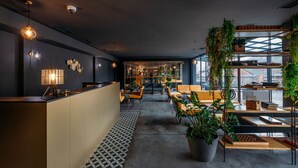 A modern interior with a reception desk, seating area, and a view of the cityscape through large windows. - Hotel Memoir Kazbegi (Kazbegi)