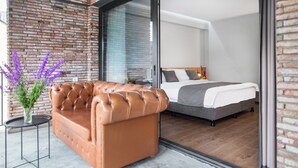 A modern hotel room with a leather sofa, a bed, and a view through a glass door. - Hotel Memoir Kazbegi (Kazbegi)