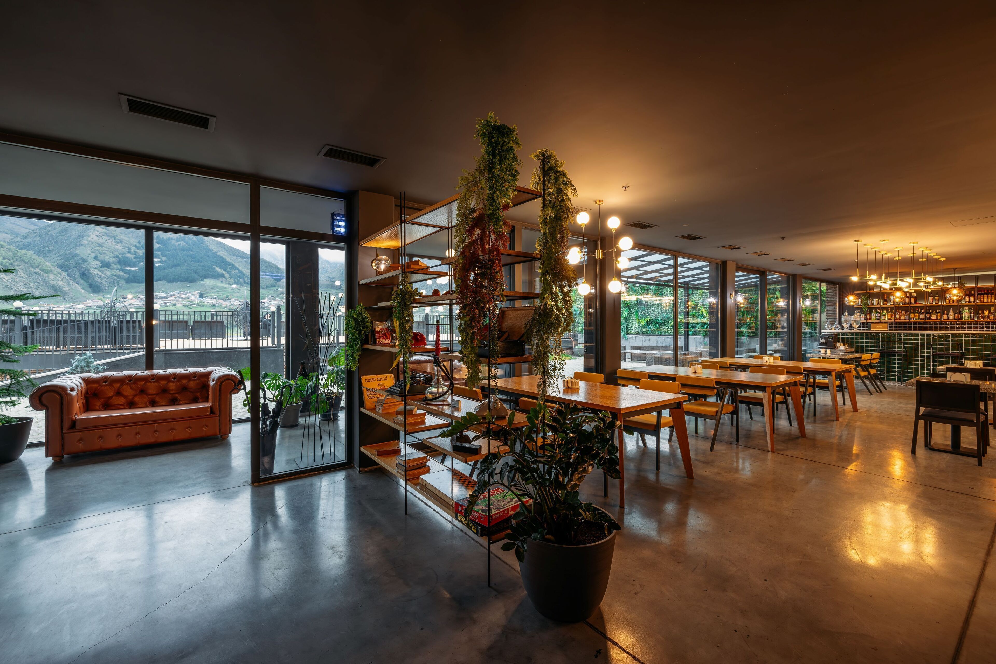 A modern interior with a sofa, bookshelves, tables, and potted plants.
