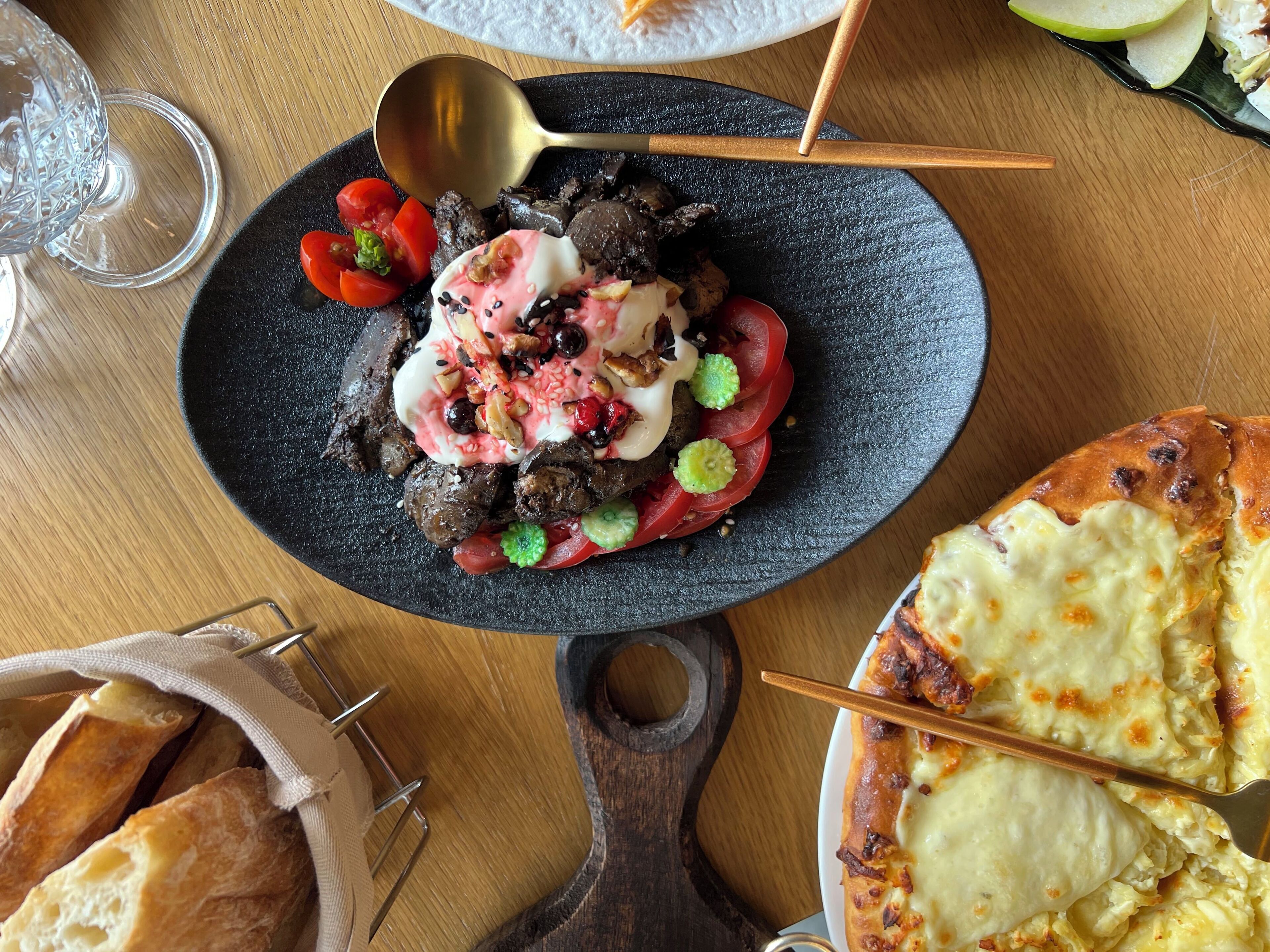 A plate of food with a spoon, a glass, and a basket of bread on a wooden table.