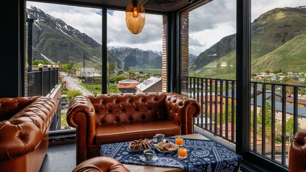 A balcony with a leather sofa and a table set with breakfast, overlooking a mountainous landscape. - Hotel Memoir Kazbegi (Kazbegi)