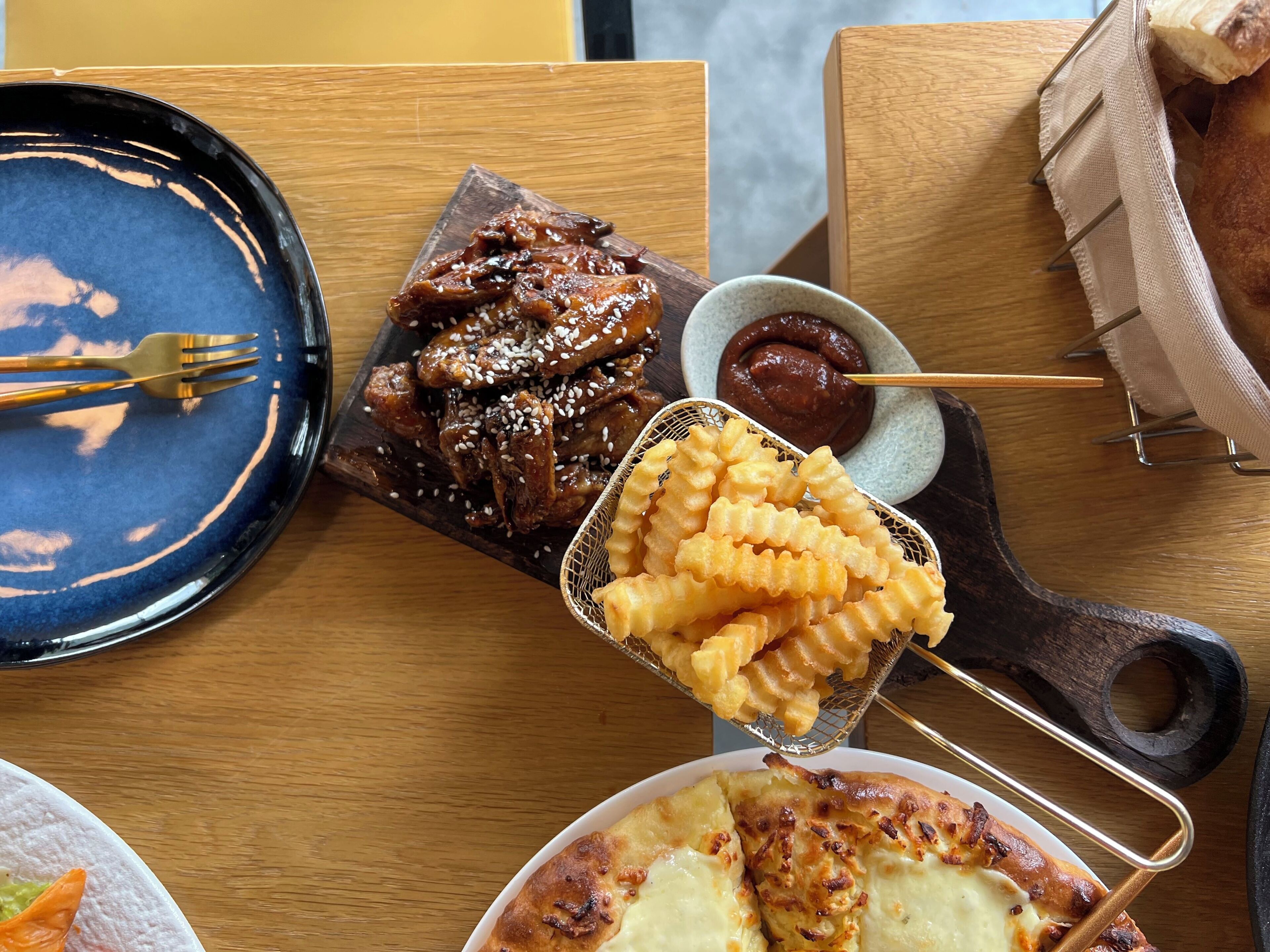 A wooden table with a blue plate, a basket of fried food, a bowl of sauce, and a fork.