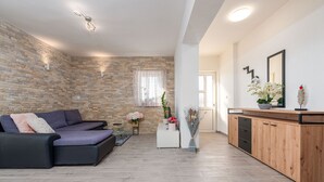 A modern living room with a stone wall, a sofa, a wooden cabinet, and a small table with flowers. - Villa Sea Pearl (Jasenice)