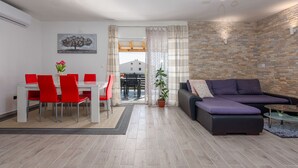 A modern living room with a sofa, dining table, and chairs. There is a potted plant and a painting on the wall. - Villa Sea Pearl (Jasenice)