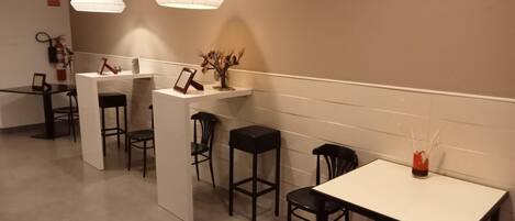 A modern, well-lit cafe with a counter, bar stools, and a table with a vase.