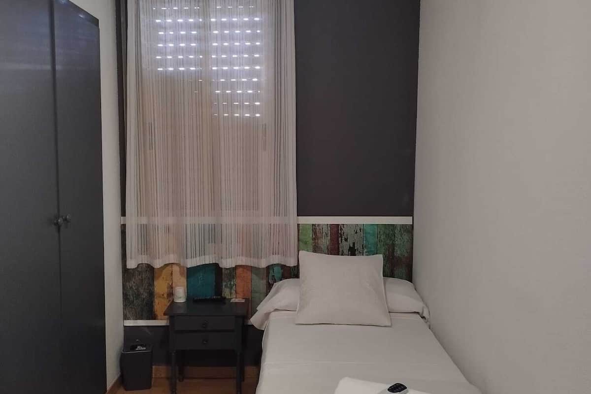 Un dormitorio pequeño y ordenado con cama, escritorio, silla y ventilador de techo.