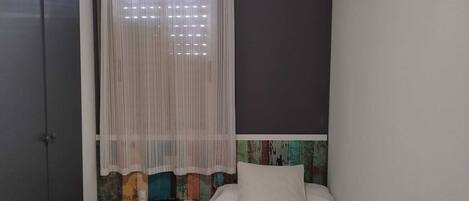 A small, neatly arranged bedroom with a bed, a desk, a chair, and a ceiling fan.