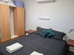 A bedroom with a bed, a wardrobe, a bedside table, and an air conditioning unit. - Foothills Vista - Guest house separate to main house-2 Adults, 1 child, 1 infant (Herne Hill)