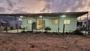 Une maison de plain-pied avec un toit plat, un porche à l’avant et une cour clôturée.