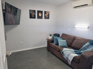 Un salon avec un canapé marron, des coussins turquoise, un mur blanc et un téléviseur à écran plat fixé au mur.