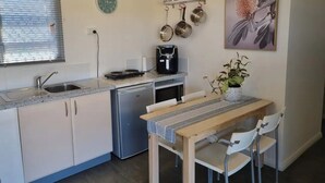 Une cuisine compacte équipée d’un évier, d’une cuisinière et d’un petit réfrigérateur. On y trouve une table à manger avec des chaises, ainsi qu’une plante en pot accrochée au mur.