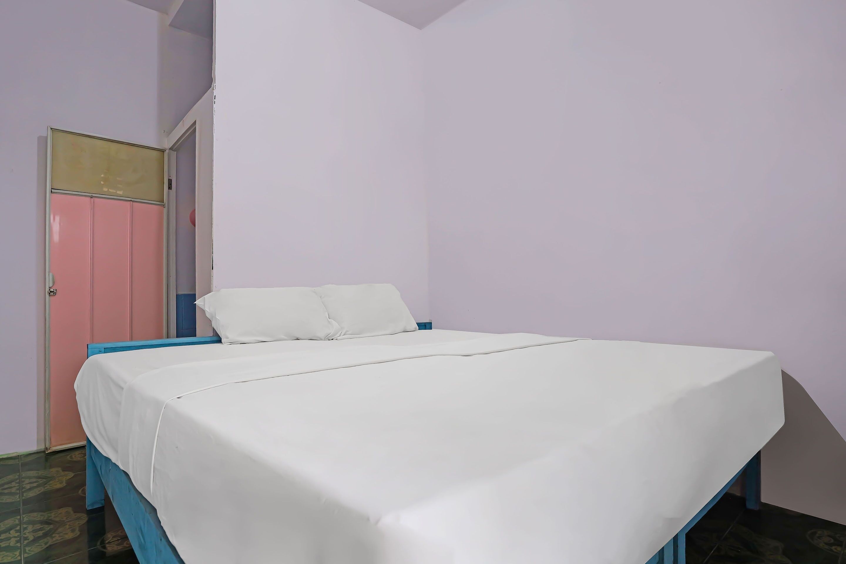 A single bed with a white mattress and blue frame in a room with light purple walls and a pink door.