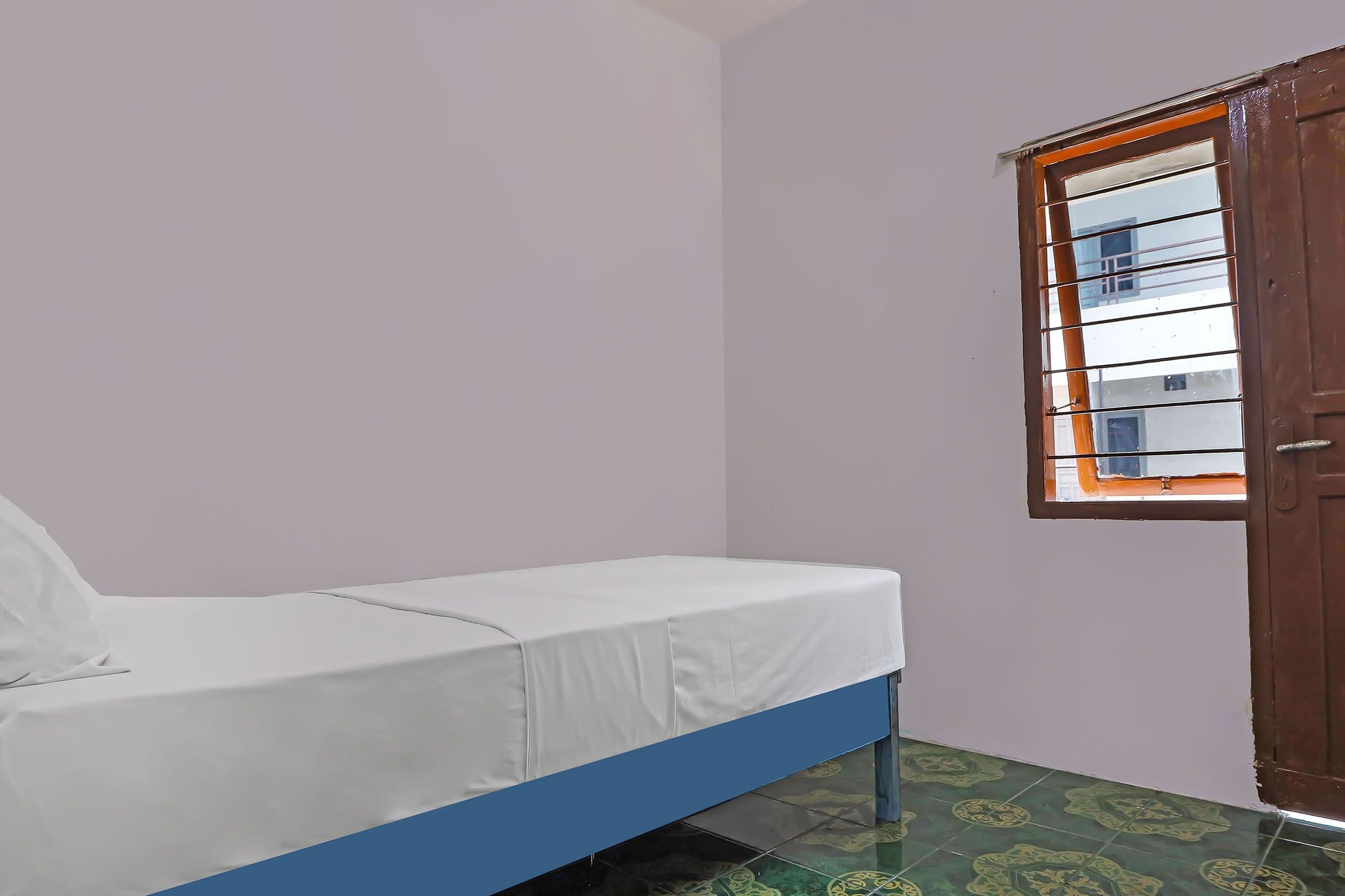 Um quarto pequeno com uma cama de solteiro, uma janela com grades e uma porta.